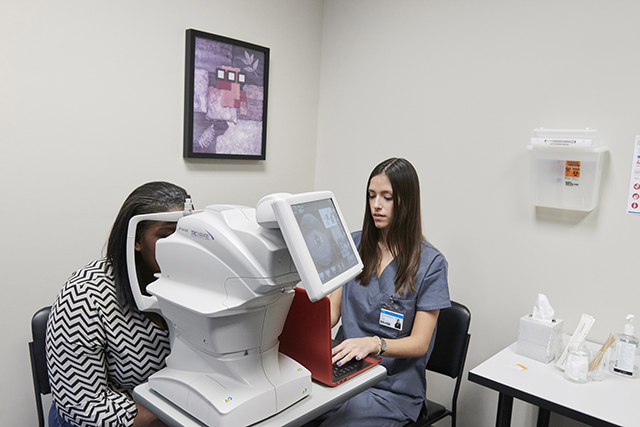 Monica typing on computer with retina on camera screen and patient leaning into camera wider view