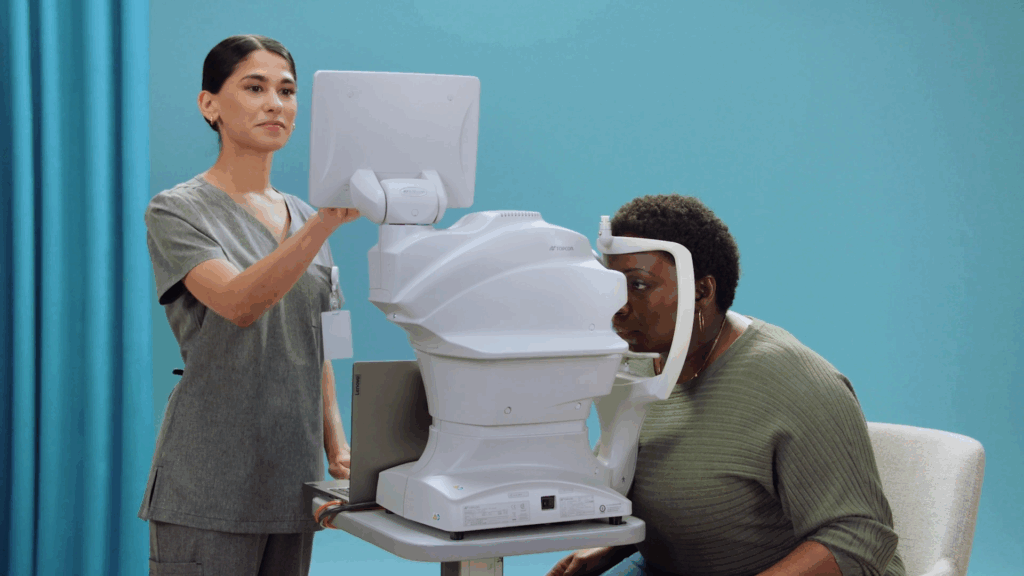 Healthcare professional operating a retinal imaging device while a patient undergoes an eye exam.